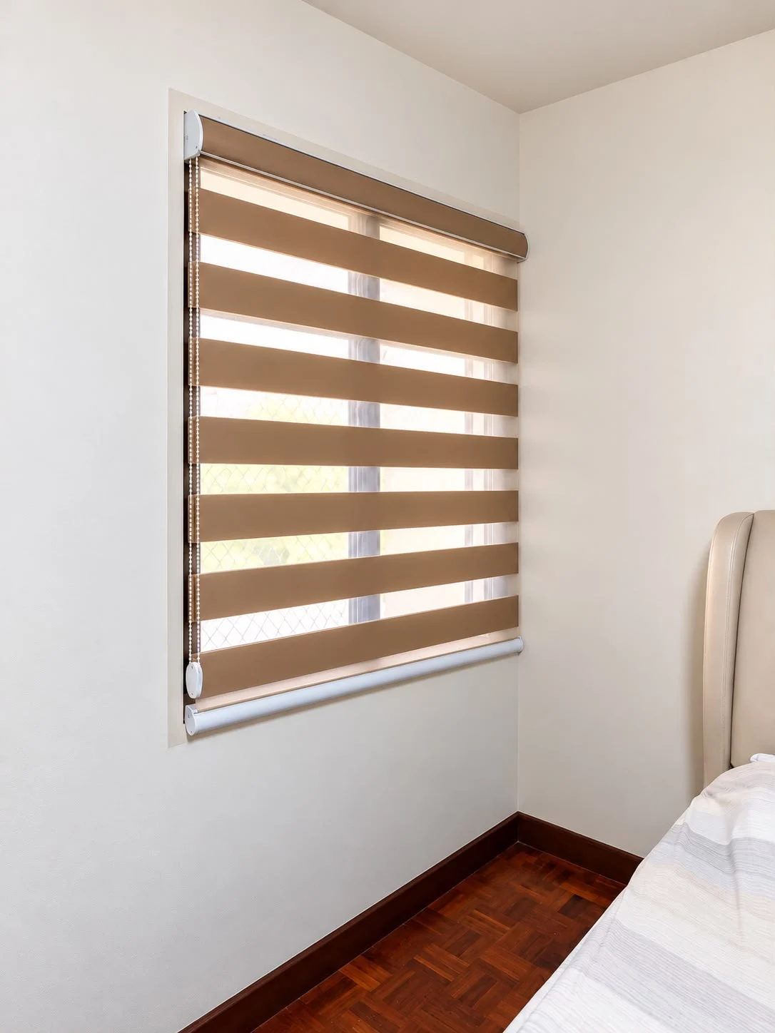 A warm brown combi blind installed beside a bed in a room with wooden flooring